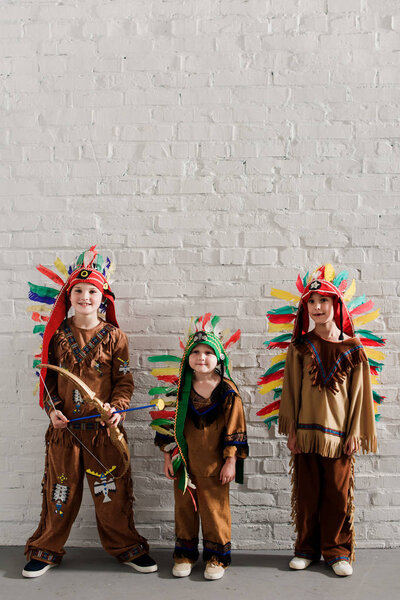 cute little boys in indigenous costumes standing against white brick wall