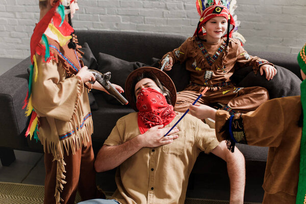 man in hat and red bandana playing together with sons in indigenous costumes at home