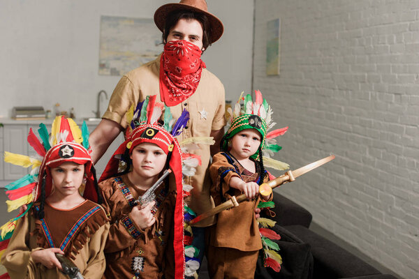 portrait of little boys in indigenous costumes and father in hat and red bandana looking at camera at home