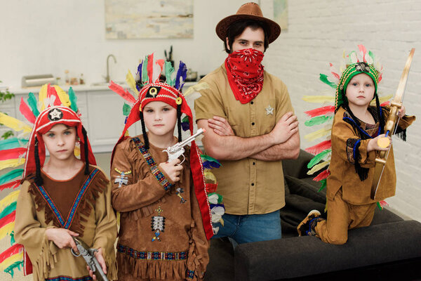 portrait of little boys in indigenous costumes and father in hat and red bandana looking at camera at home