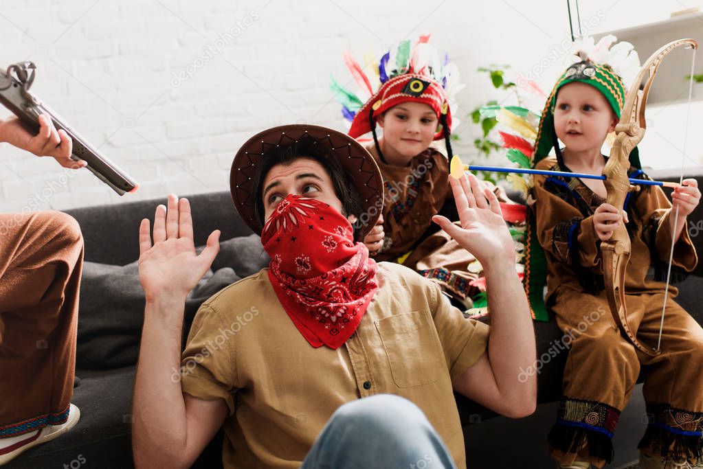 man in hat and red bandana playing together with sons in indigenous costumes at home