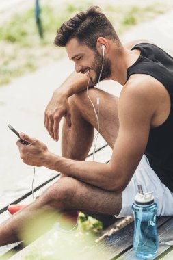 sporcu şişe su smartphone ve spor Bahçesi, bankta kulaklık ile müzik dinleme