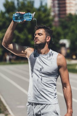 athletic young man pouring water on himself after training