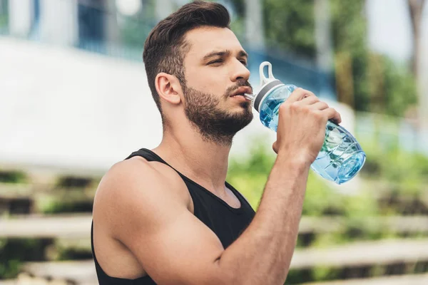 ボトルから水を飲む若いスポーツマンの側面図 — ストック写真