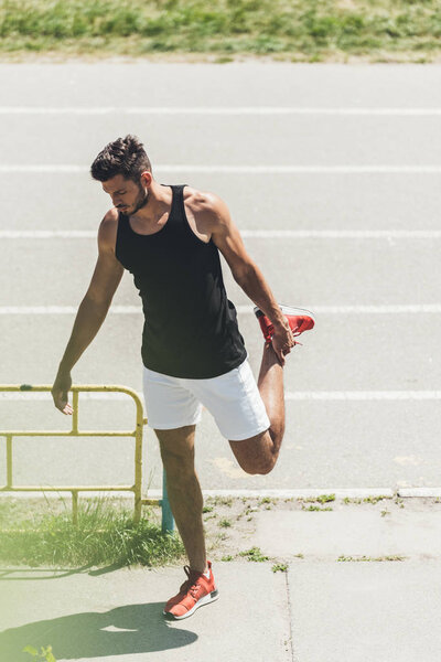 young male athlete stretching near running track at sport playground 