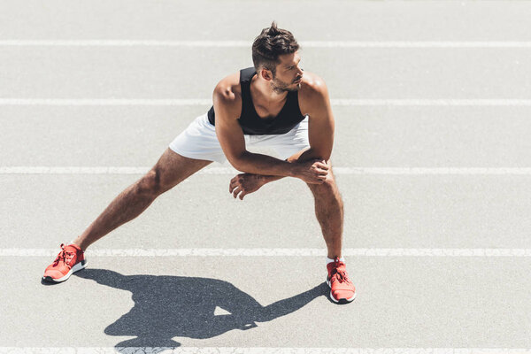 young male jogger stretching on running track at sport playground 