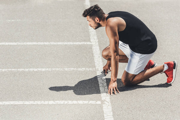 side view of young male athlete on low start on running track 