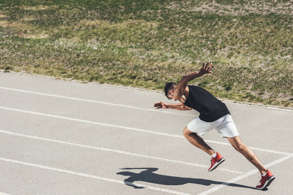 young male sprinter taking off from starting position on running track