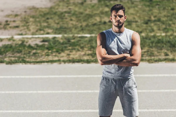 confident sporty young man with crossed arms looking at camera on running track