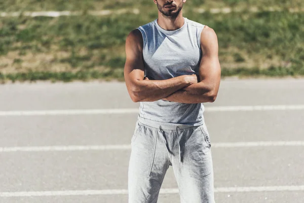 cropped shot of sporty young man with crossed arms on running track