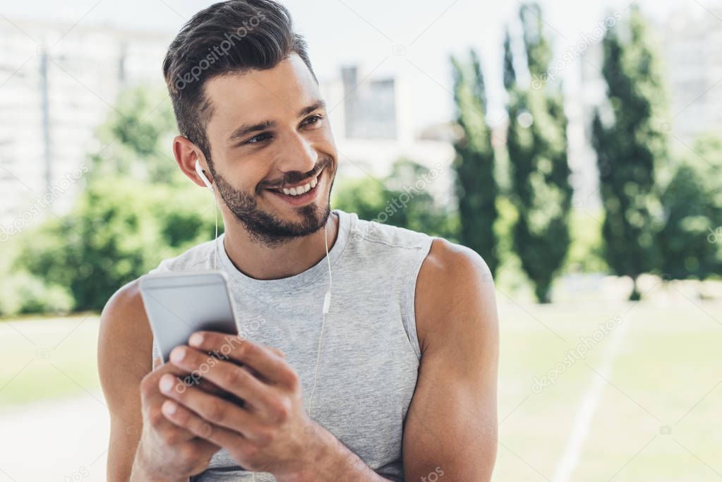 close-up portrait of handsome young man listening music with smartphone and earphones outdoors