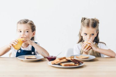 güzel küçük tost reçelli yeme ve üzerinde beyaz izole kahvaltı için portakal suyu içme kız kardeş