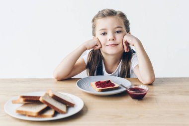 tost ve üzerinde beyaz izole kamera bakarak kahvaltıda reçeli ile gülümseyen küçük kız öğrenci