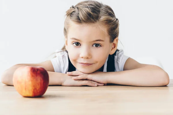 Malá Školačka Sedí Stolu Červeným Apple Při Pohledu Fotoaparát Izolované — Stock fotografie