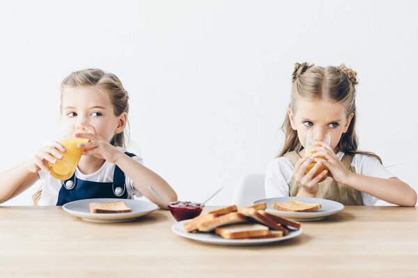 beautiful little sisters eating toasts with jam and drinking orange juice for breakfast isolated on white