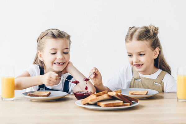 adorable little sisters eating toasts with jam for breakfast isolated on white
