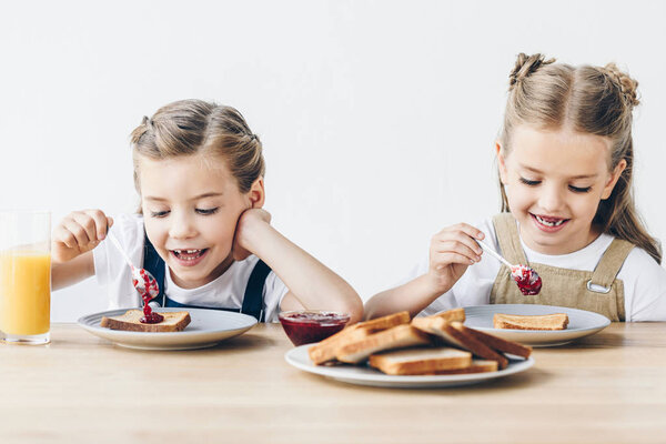 happy little sisters eating toasts with jam for breakfast isolated on white