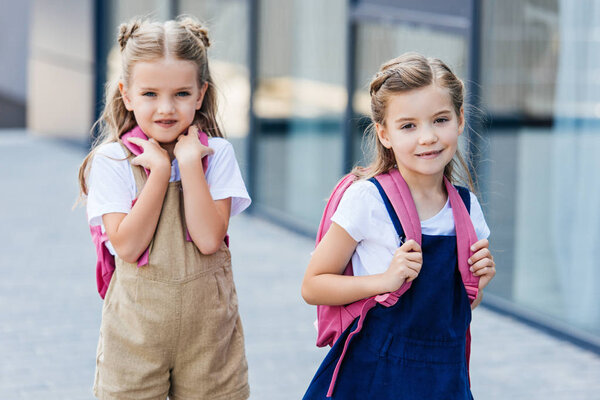 adorable little schoolgirls with pink backpacks walking on street