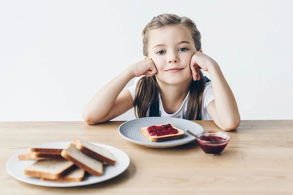 smiling little schoolgirl with toasts and jam for breakfast looking at camera isolated on white
