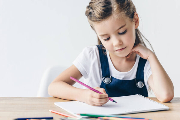 concentrated little schoolgirl drawing with color pencils isolated on white