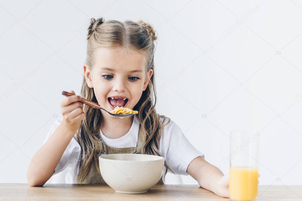 excited little schoolgirl eating healthy breakfast isolated on white