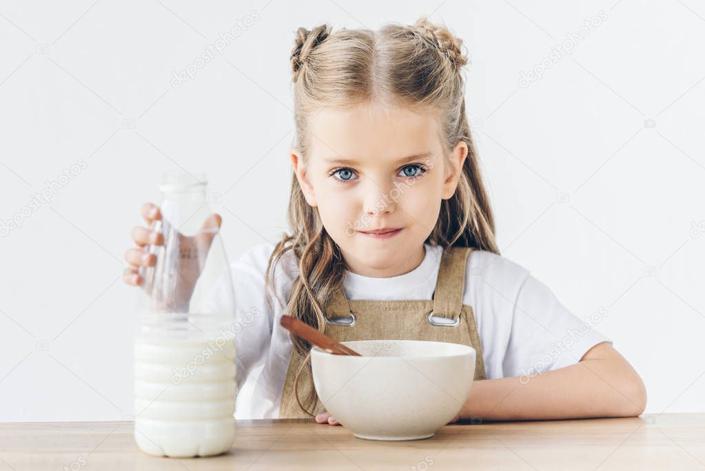 cute little schoolgirl with bowl of cereal and bottle of milk isolated on white