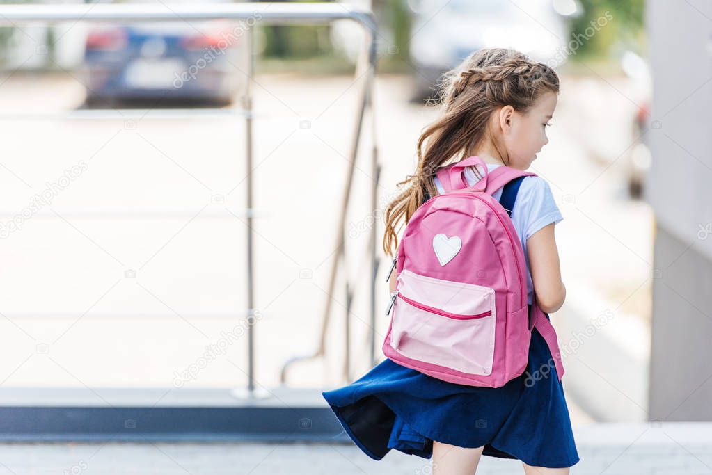 rear view of little schoolgirl with backpack on street