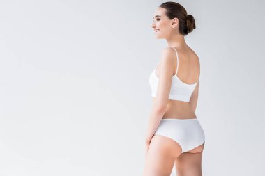 Beyaz iç çamaşırı gri arka plan üzerinde izole gülümseyen çekici beyaz kadın yan görünüm 