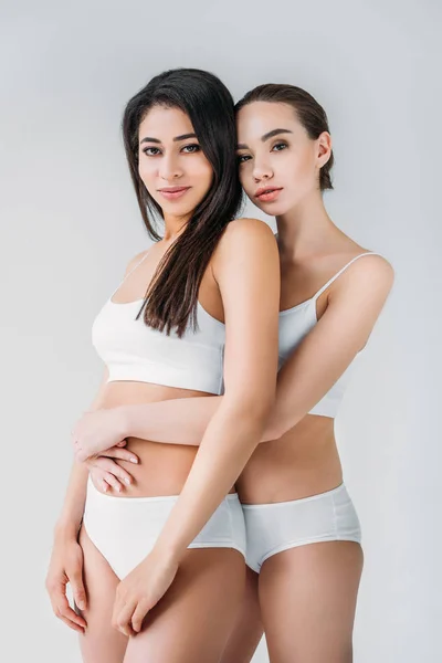 Två Leende Mångkulturella Kvinnor Vita Underkläder Embracing Isolerade Grå Bakgrund — Stockfoto