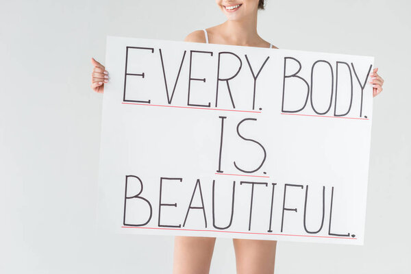 Cropped image of smiling woman holding banner with lettering every body is beautiful isolated on gray background