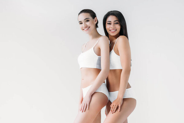 smiling attractive multicultural women posing in white lingerie isolated on gray background 