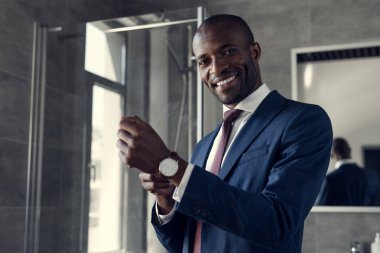 happy young businessman putting on his wristwatch at bathroom clipart