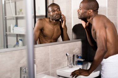 çekici bir genç adam, banyo aynada bakarken cilt netliğini inceleyerek