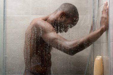 side view of handsome young african american man washing body in shower  clipart