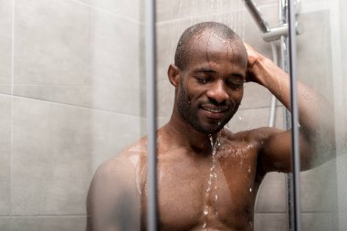 handsome smiling african american man with closed eyes taking shower clipart