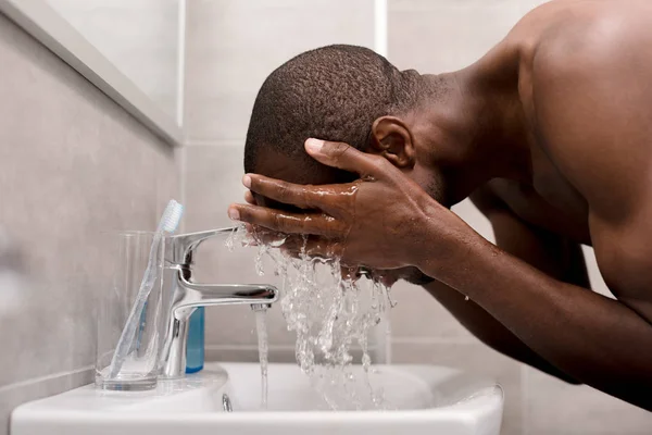 朝の洗面所で彼の顔を洗う若い男の側面図 — ストック写真