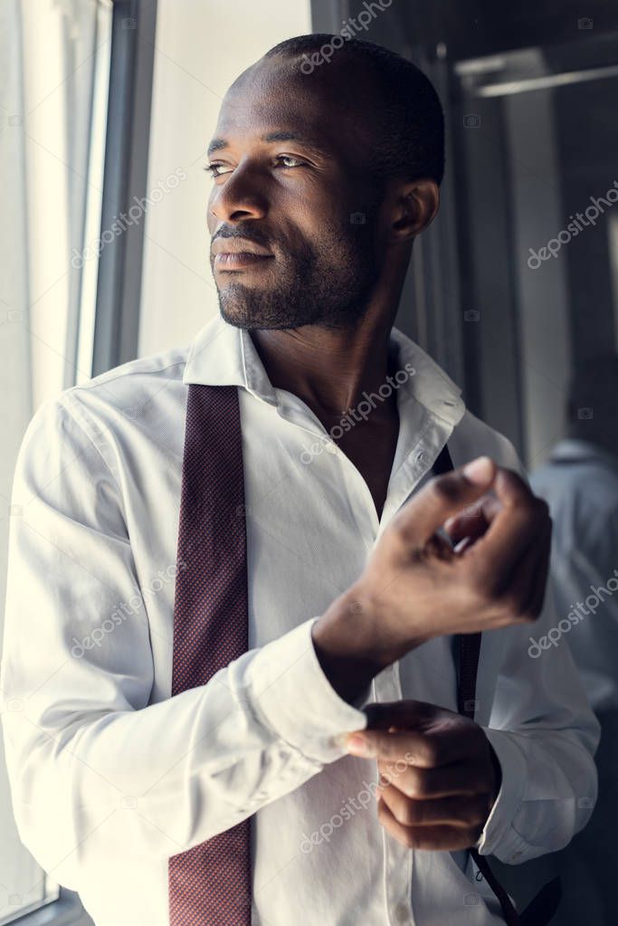 close-up portrait of thoughtful young businessman in white shirt buttoning cufflinks and looking away