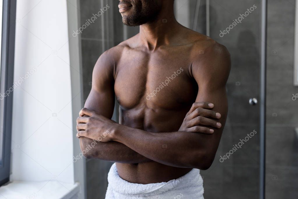 cropped shot of smiling african american man in towel standing with crossed arms in bathroom