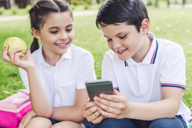 çimenlerin üzerinde otururken Smartphone birlikte kullanarak okul gülümseyen