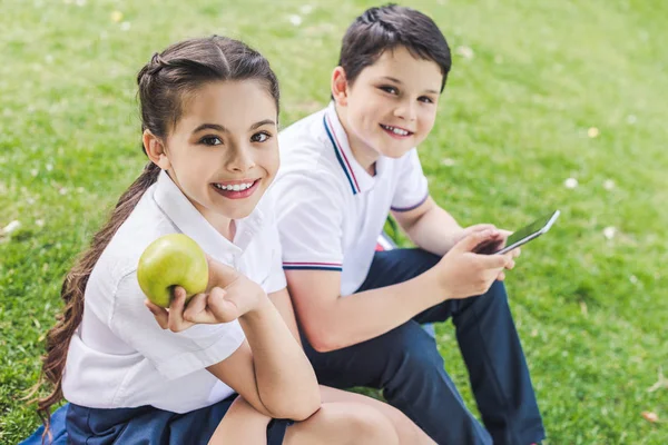 Schoolchildren Using Smartphone Together While Sitting Grass Looking Camera — Stock Photo, Image