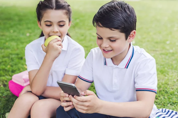 Счастливые Школьники Используют Смартфон Вместе Сидя Траве — стоковое фото