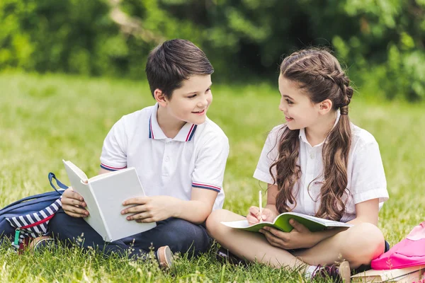公園の芝生の上に座って一緒に宿題をやって幸せな小学生 — ストック写真