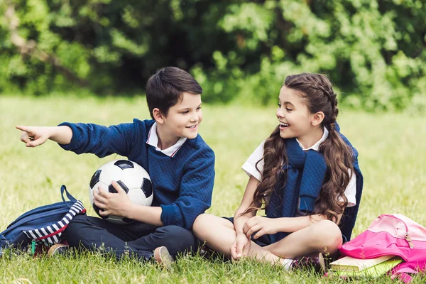 Šťastné Děti Sedí Trávě Parku Batohy Fotbalový Míč Chatování — Stock fotografie