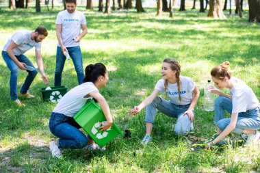 young volunteers with recycling boxes cleaning lawn in park clipart