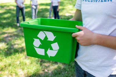 cropped view of volunteer holding green recycling box in park   clipart