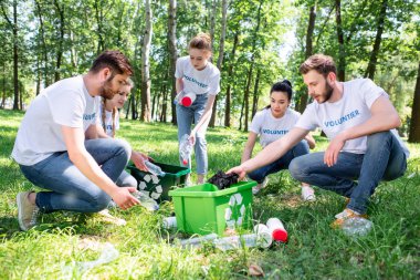 young volunteers with green recycling box cleaning park together clipart
