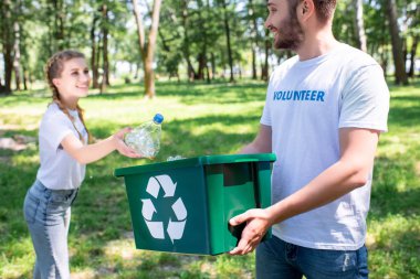 young couple of volunteers with green recycling box cleaning park  clipart