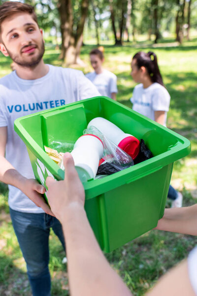 волонтеры-мужчины с зеленой коробкой для переработки отходов в парке
 