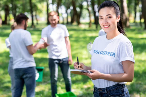 Chica Escribiendo Libro Texto Mientras Voluntarios Limpieza Parque — Foto de Stock