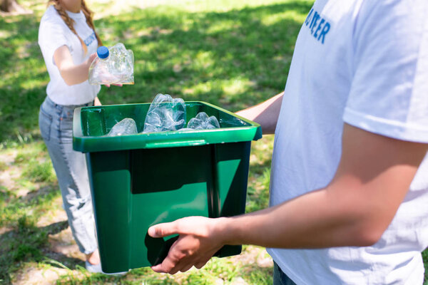 cropped view of couple of volunteers with recycling box cleaning park 